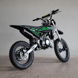A black and green mini dirt bike with off-road tires, a black exhaust, and silver forks, photographed in a studio setting against a neutral gray background.