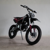 A black and silver dirt bike with red flame graphics and the number 65 on the front fender, photographed on a concrete floor against a plain light gray wall.