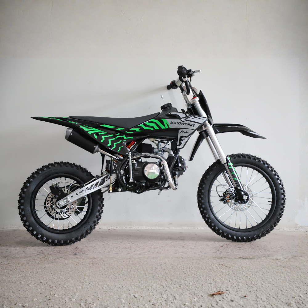 A black and silver mini dirt bike with bright green graphic decals, photographed from the side against a plain concrete wall and floor.