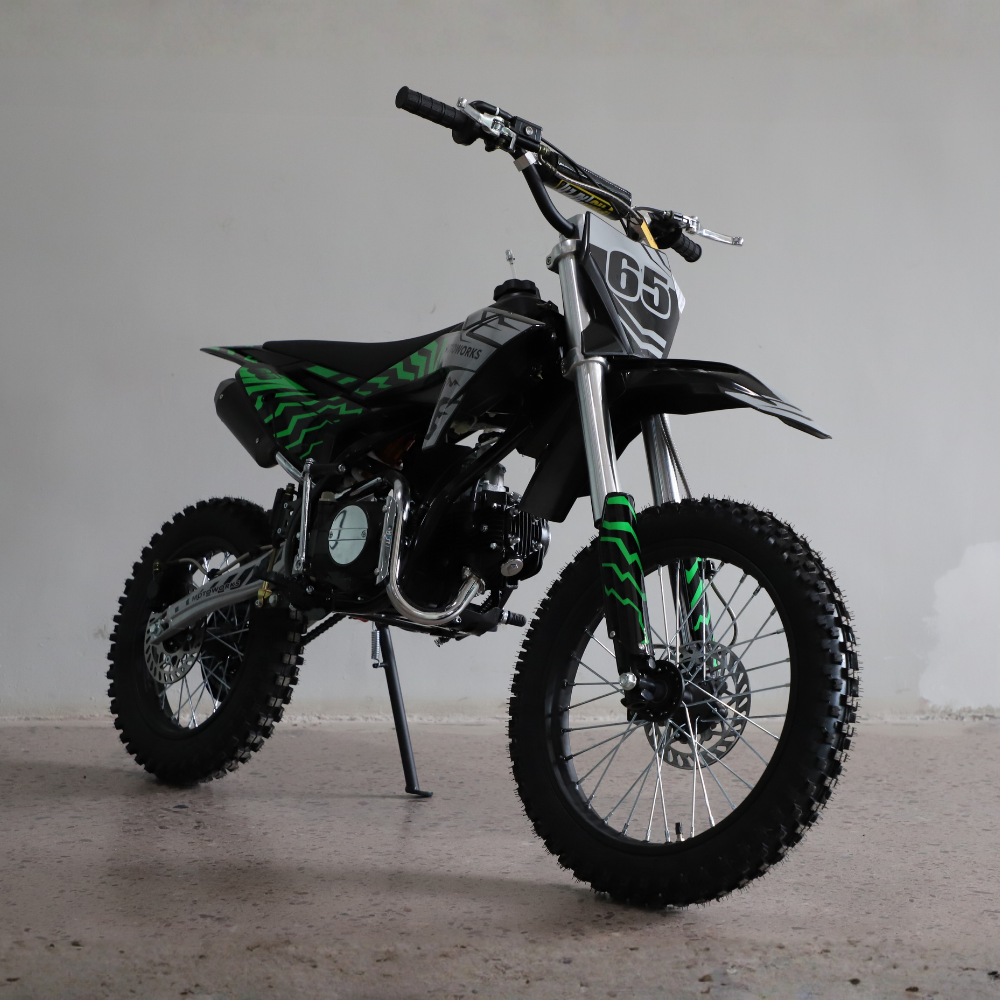 A black and green mini dirt bike with a number 65 plate, standing on its kickstand in a studio setting.