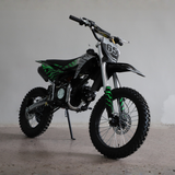 A black and green mini dirt bike with a number 65 plate, standing on its kickstand in a studio setting.