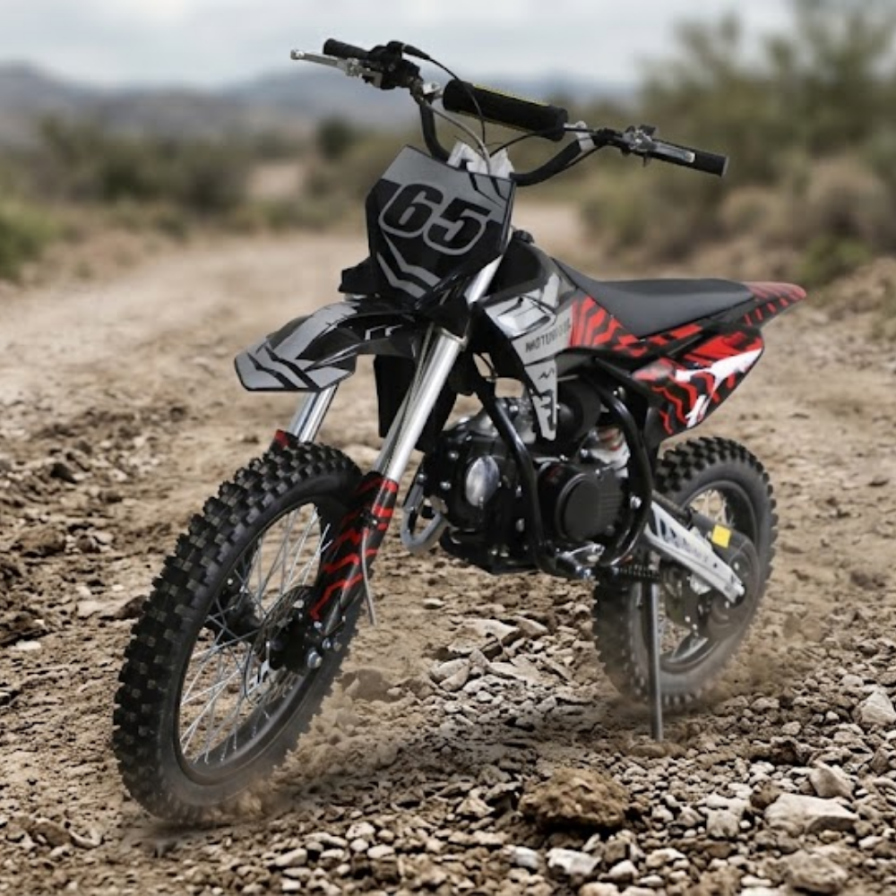 A youth dirt bike with a black, white, and red color scheme, standing on a rocky dirt trail in an outdoor desert setting.