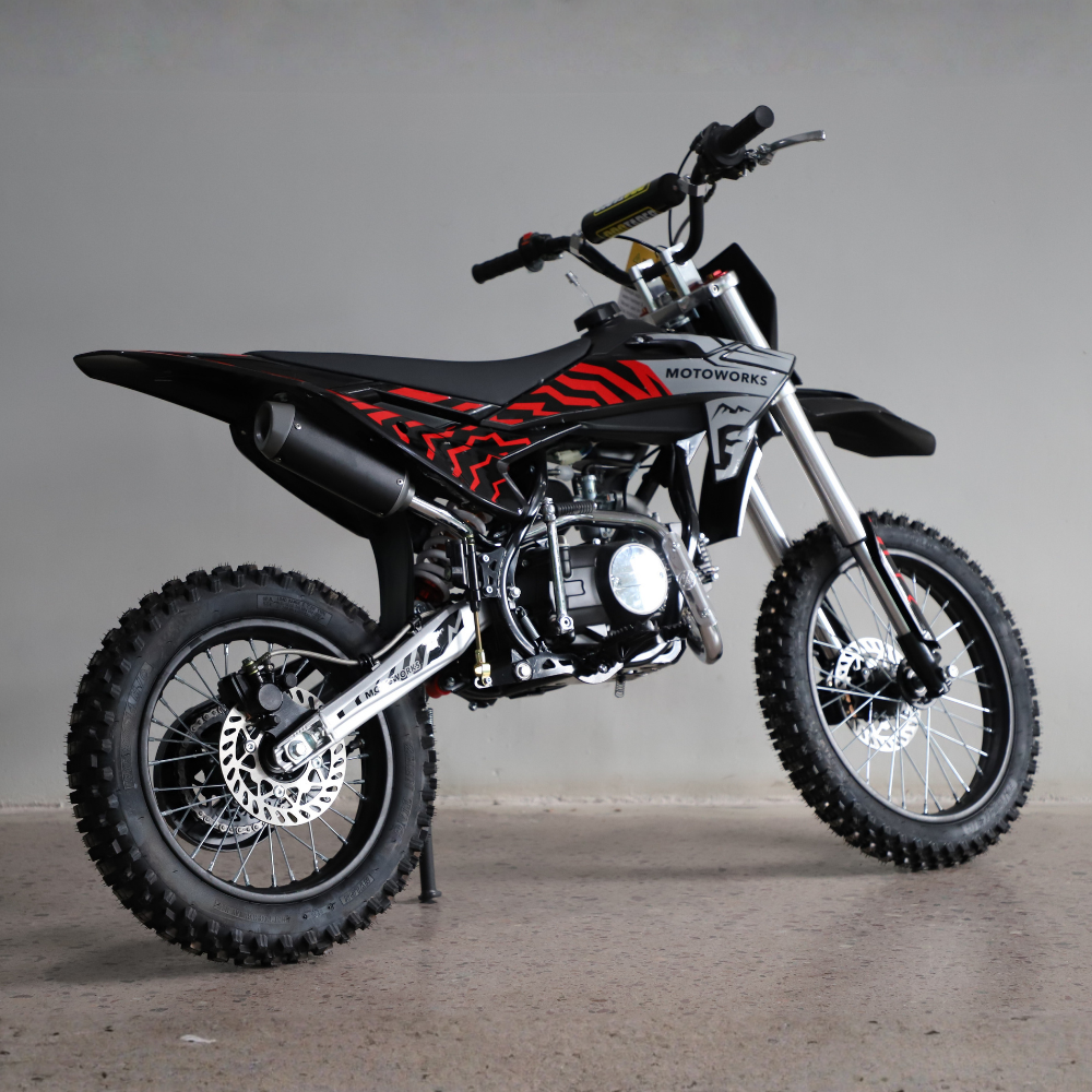 A black and red off-road dirt bike with knobby tires, a silver engine, and a black exhaust, photographed in a studio setting against a neutral gray background.