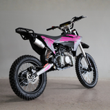 A pink and black mini dirt bike with knobby tires, photographed from a three-quarters angle against a neutral gray studio background.