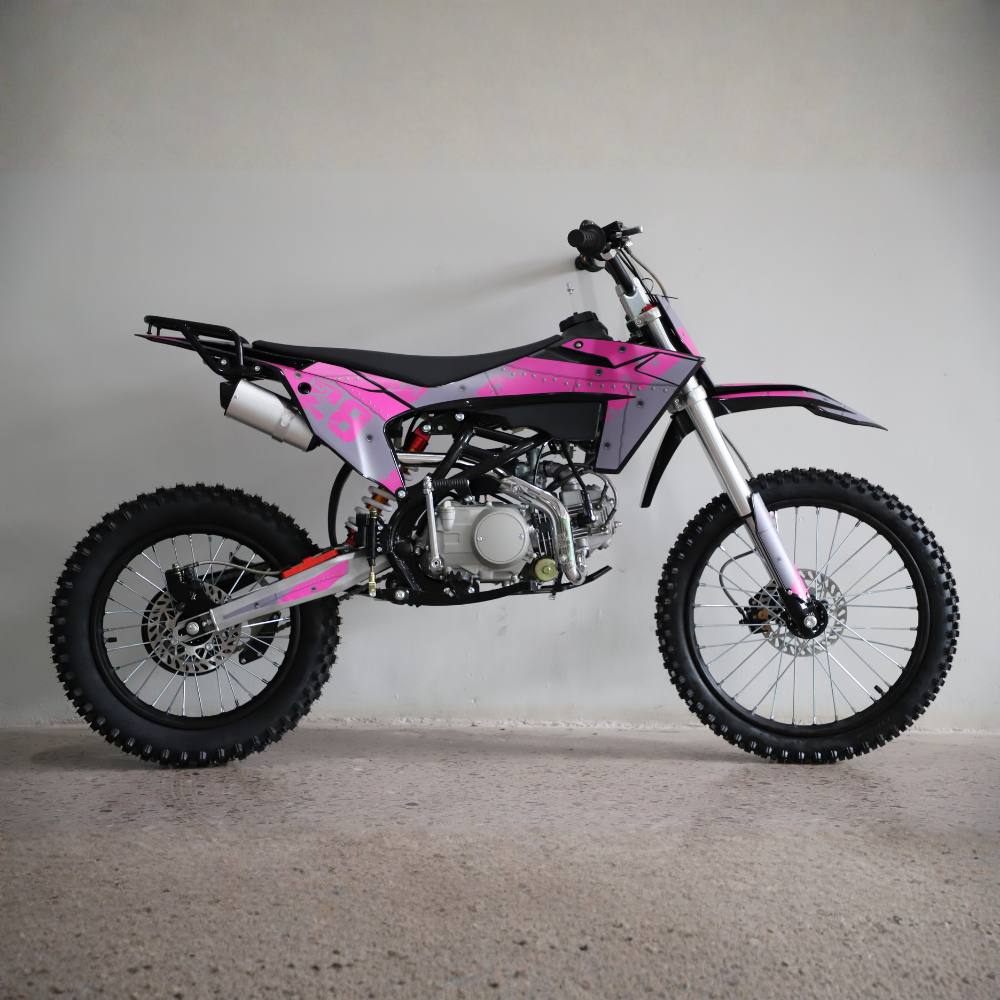 A pink and black mini dirt bike with knobby tires, photographed in profile against a plain light gray wall and concrete floor.