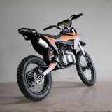 An off-road dirt bike with a black and orange color scheme, featuring knobby tires, a rear luggage rack, and a silver exhaust pipe, photographed in a studio setting.