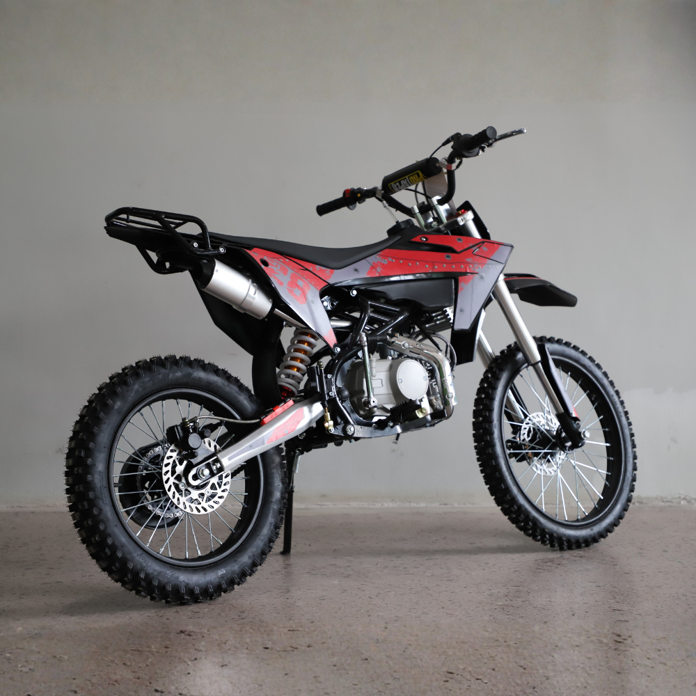 A red and black off-road dirt bike with a silver exhaust and knobby tires, photographed on a concrete floor against a plain gray wall.