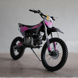 A pink and black mini dirt bike with knobby tires, photographed on a concrete floor against a plain gray wall.