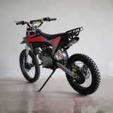 A small off-road dirt bike with red, black, and gray graphics, photographed on a light gray concrete floor against a plain light gray wall.