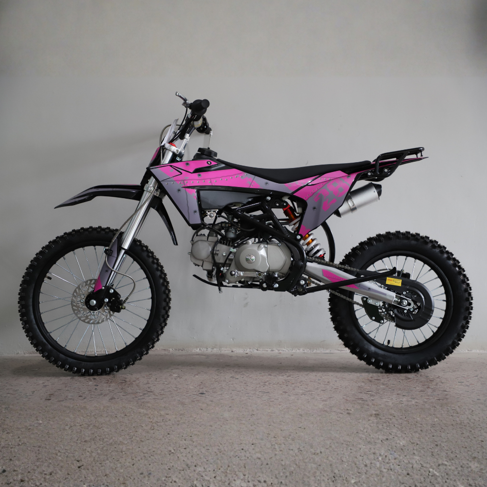 A pink and black mini dirt bike with knobby tires, photographed from the side against a plain gray wall and concrete floor.