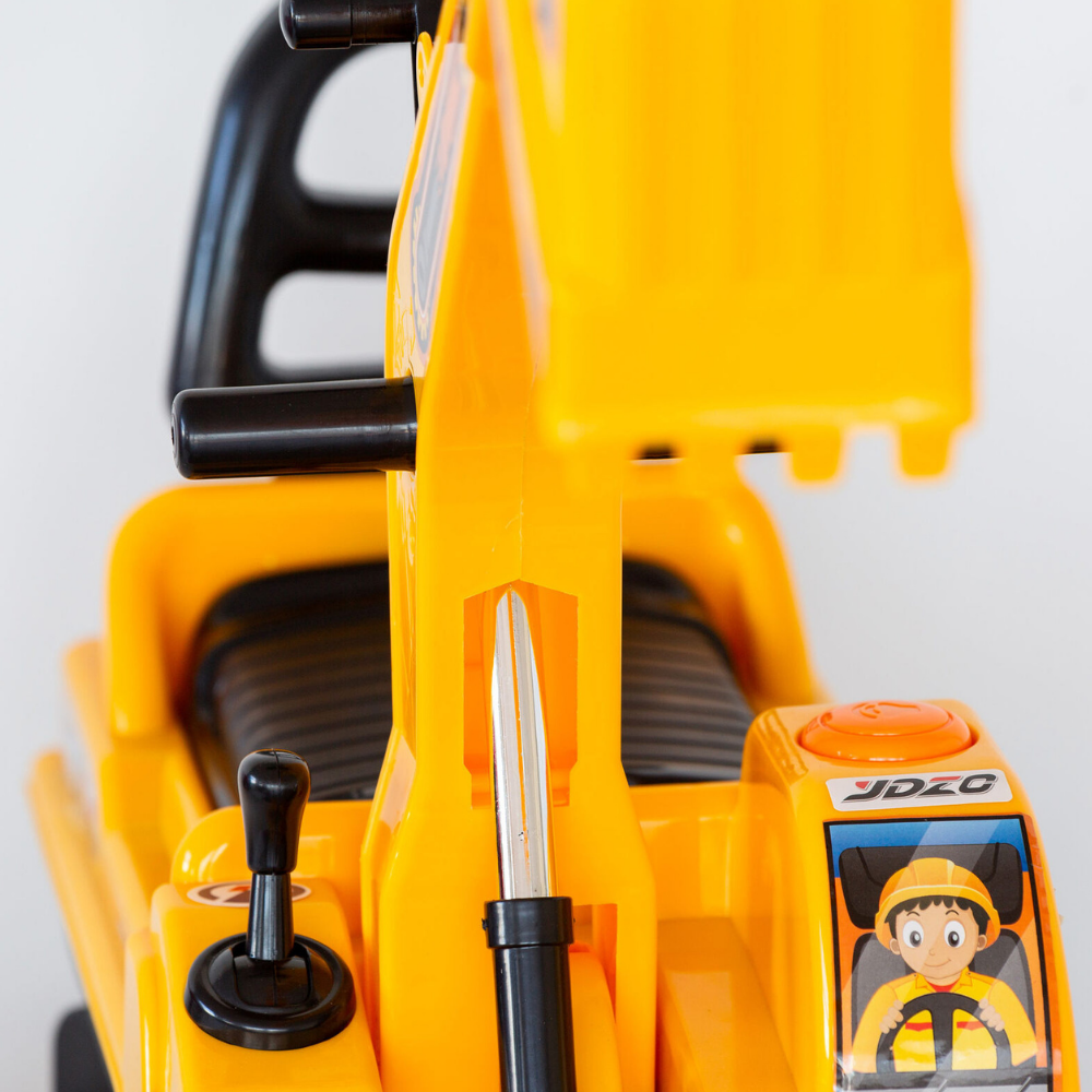 Close-up of a yellow toy excavator with black controls, a small driver window showing a cartoon character, and a metal digging arm attachment.