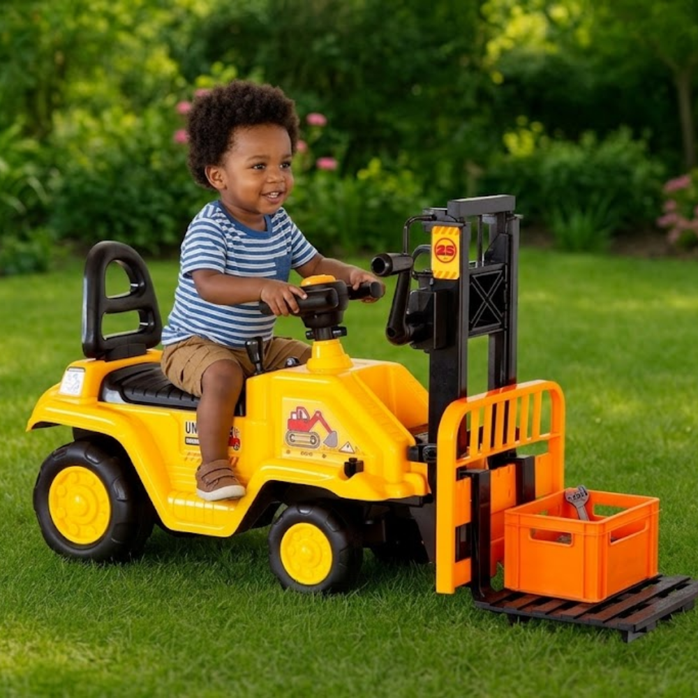 A young child sitting on a yellow ride-on toy tractor with a black steering wheel and an orange front loader bucket, photographed outdoors on a green lawn with garden foliage in the background.