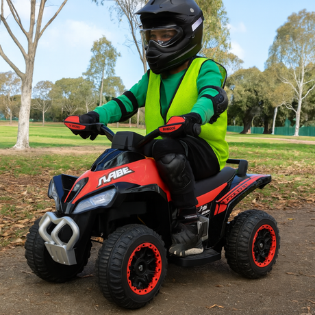 Child on a red and black toy ATV in a park