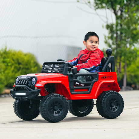 A young boy sitting inside a red Jeep-inspired remote-controlled ride-on electric car outdoors, smiling while holding the steering wheel