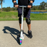 Person riding a scooter with rainbow-colored wheels in an outdoor setting
