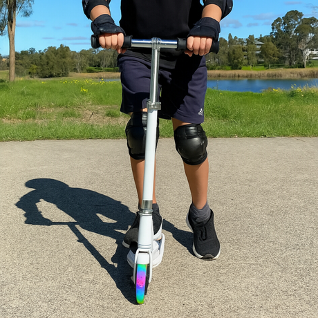 Person riding a scooter with rainbow-colored wheels in an outdoor setting