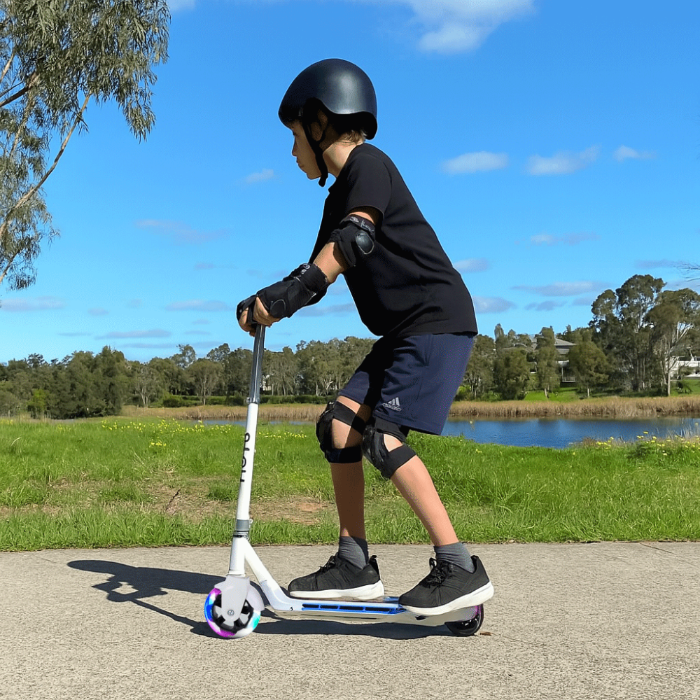 Child riding a scooter outdoors with a helmet and protective gear on a sunny day.