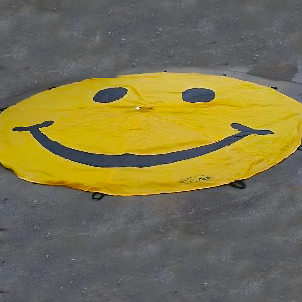 Yellow parachute with a large black smiley face, laid flat on a grey surface