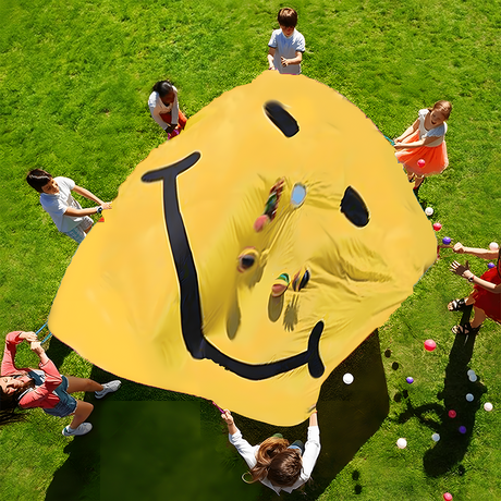 Children holding up a yellow parachute with a black smiley face, while tossing colourful balls into the air