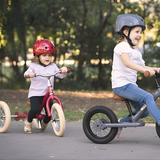Two children riding balance bikes outdoors with helmets on.