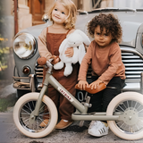 Two children with a balance bike in front of a vintage car.