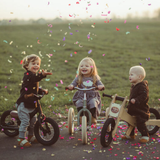 Three children on balance bikes with confetti in a field