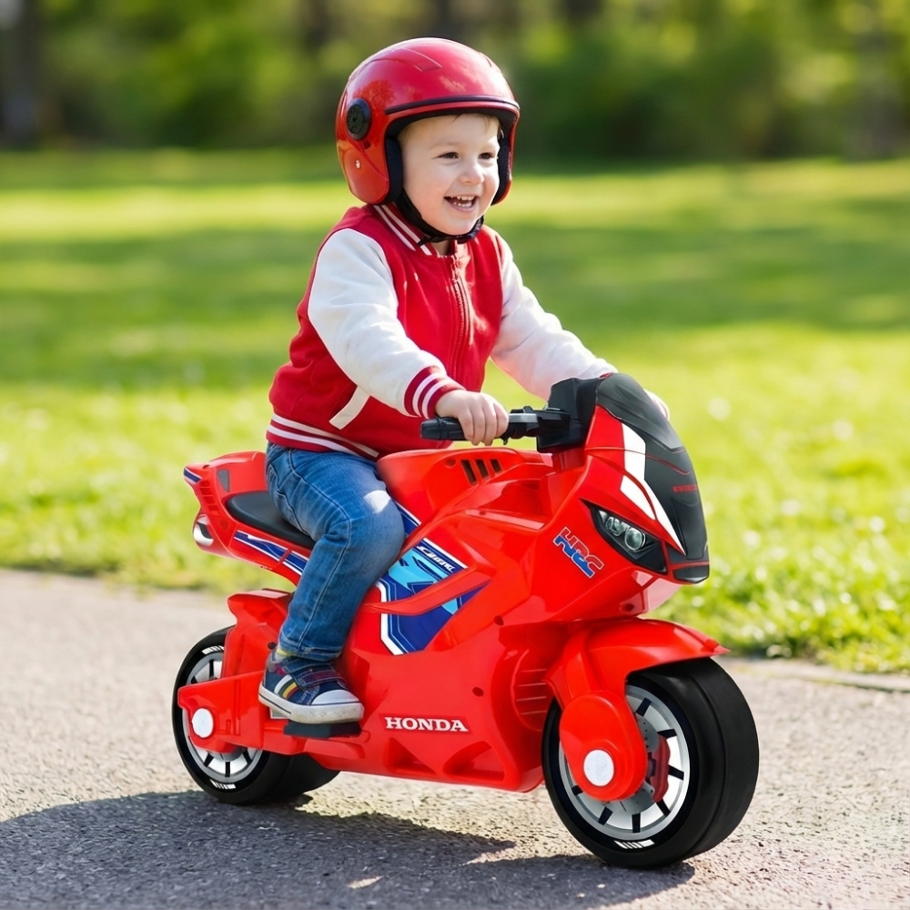 Child riding a red Honda toy motorcycle on a sunny day.