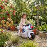 Child on a toy motorcycle in a garden setting