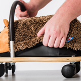 Person using a small wheeled cart with a plush toy on a light background