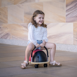 Young girl riding a colourful toy bug on a stone floor with a patterned wall in the background