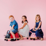 Three children sitting on colorful toy cars against a pink background