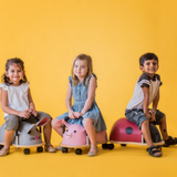 Three children sitting on colorful animal-shaped chairs against a yellow background