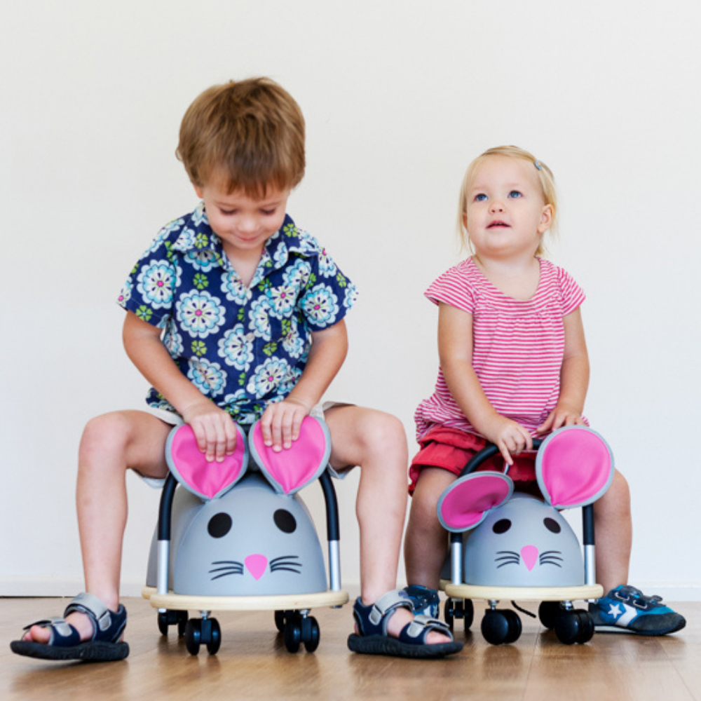 Two children sitting on mouse-shaped chairs with pink ears on a plain background