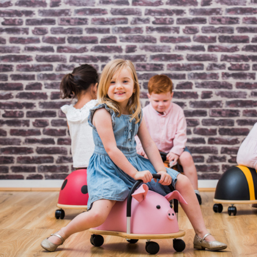 Children playing with colorful ride-on toys against a brick wall.