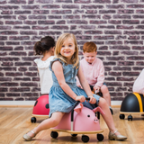 Children playing with colorful ride-on toys against a brick wall.