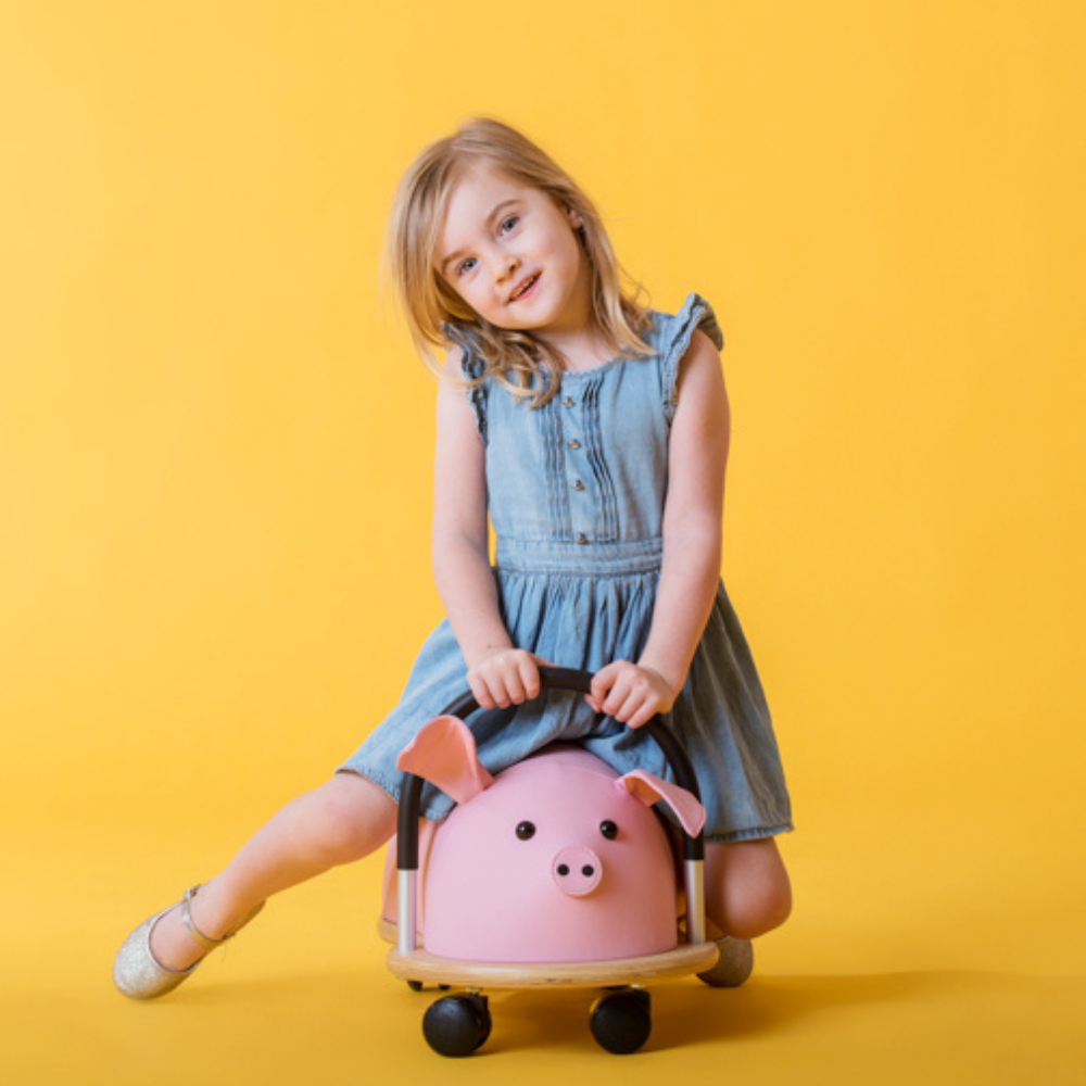 Child sitting on a pink pig-shaped toy against a yellow background