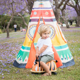 Child playing with a toy car in front of a colorful teepee in a park.