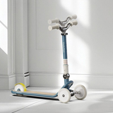 Children's scooter with a blue handlebar and white wheels on a light gray floor.