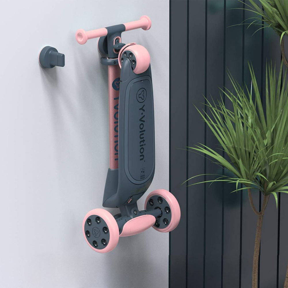 Children's scooter with pink and black design leaning against a wall next to a plant.