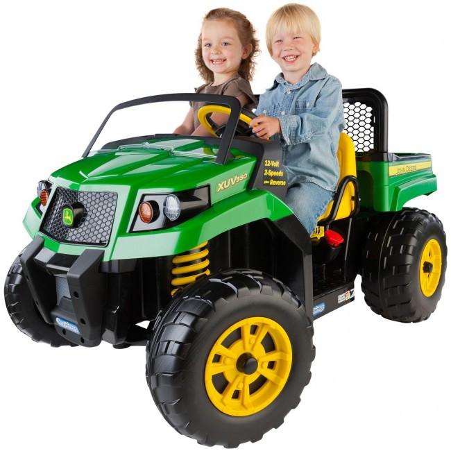 Two smiling children sitting in a green ride-on John Deere XUV toy vehicle, featuring large yellow wheels and realistic detailing, including headlights and a roll bar